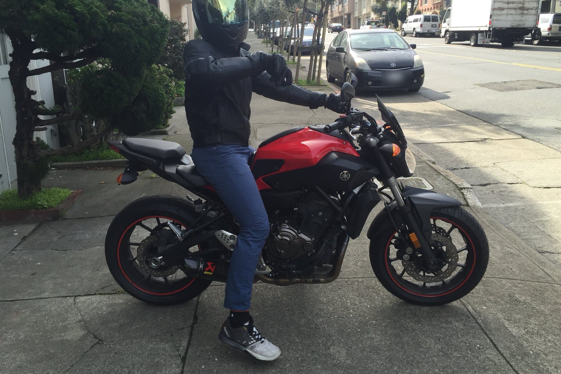 Daniel in a helmet and leather jacket on his red-and-black Yamaha FZ-07, parked on a San Francisco sidewalk